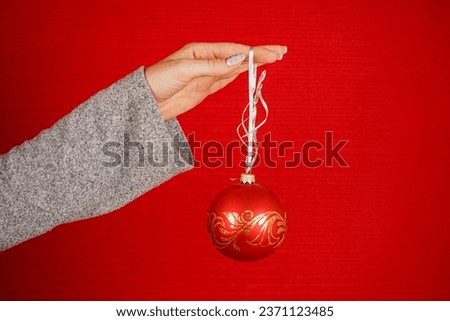 Red round Christmas tree ball in female hand isolated on red background. A woman's hand holds a decorative Christmas tree toy. New Year and Christmas concept. Holiday, decorating the Christmas tree