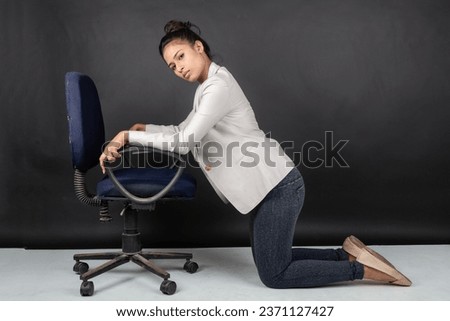 Cheerful young female model in casual wear wearing white jacket, black top and black jeans posing with a chair. Shoot for advertisement.