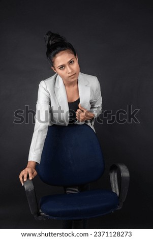 Cheerful young female model in casual wear wearing white jacket, black top and black jeans posing with a chair. Shoot for advertisement.