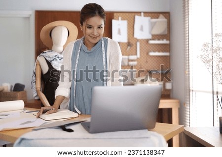 Fashion seamstress woman checking sketch of fashion clothes and reading information on laptop
