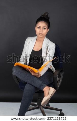 Exhausted and worried young female model in casual wear wearing white jacket, black top and black jeans sitting on a chair holding a folder. Shoot for advertisement.