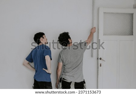 Two young beautiful Caucasian plasterers in work clothes and with brown hair hold large spatulas in their hands and check the evenness of the wall after puttying in the room near the door, close-up si