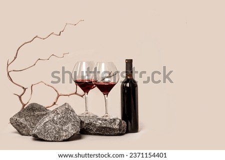Two glasses of red wine on stones and a bottle on a beige background with copy space for text.