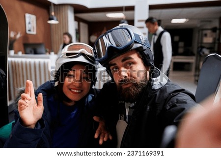 Young guests capturing winter adventures with selfies on smartphone. Blend of technology and vacation in wintertime for couple in snow clothing ski goggles and helmet at exclusive mountain resort.