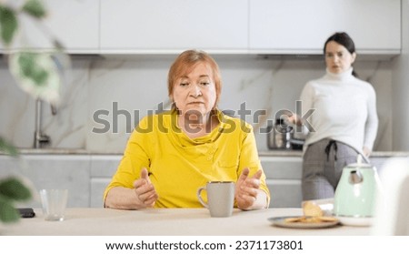 Distressed mature woman after a conflict with her daughter sitting at the table in the home kitchen Royalty-Free Stock Photo #2371173801