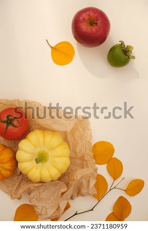 Minimal style, advertising photo with romantic autumn decoration with dried yellow leaves, pumpkins, tomatoes and apples on a beige background. Blank space for design