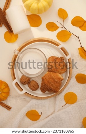 Photo of a snack with warm autumn concept. On the tray are delicious croissants and a glass of hot milk. Dried yellow leaves stand out, decorated with pumpkins and white candles