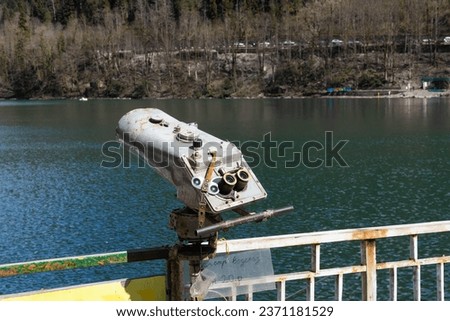 Vintage metal binoculars in mountain Ritsa lake in Abkhazia, Georgia. Tourist telescope against blurred water background. Binoculars for sightseeing. Translation: Inspection of the waterfall
