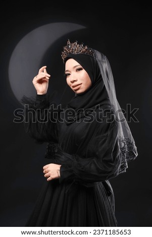 Beautiful Asian in black dress and hijab over dark background. Dark princess.