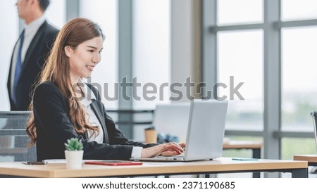 Portrait shot of Asian professional successful female businesswoman secretary employee in formal suit sitting smiling look at camera typing laptop notebook computer at working desk in company office.