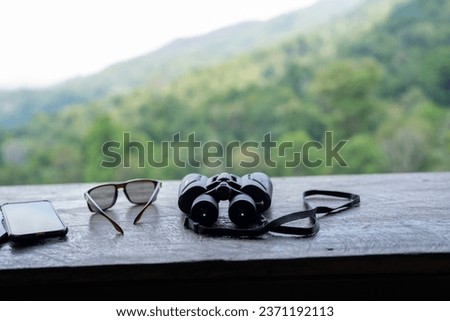 Travel equipment includes binoculars, cell phones, and sunglasses. On a wooden table, green background.
