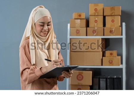 Small Business Startup, SME Owner, Muslim Woman Entrepreneur, Islam Counts Parcel Boxes and Verifies Online Orders to prepare packs and deliver to customers independent business idea.