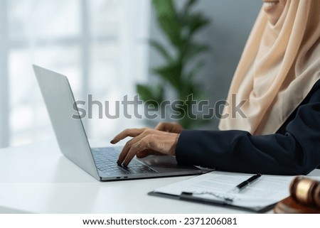 female lawyer Muslim wearing hijab working on business contract documents with laptop and reading law book Take notes to check the accuracy of justice. Legal services concept in the office.