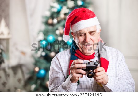 Senior man looking at display of retro style camera and smiling against Christmas background 