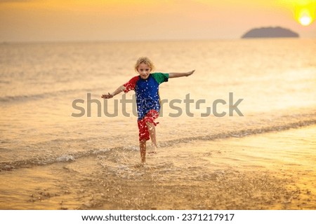 Child playing on ocean beach. Kid jumping in the waves at sunset. Sea vacation for family. Little boy running on exotic island during summer holiday. 