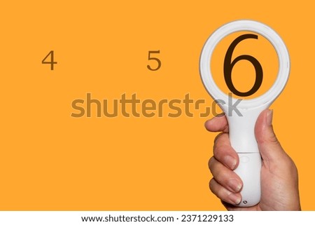 The number 6 seen enlarged through a magnifying glass. An Orange background with plenty of copy space. 