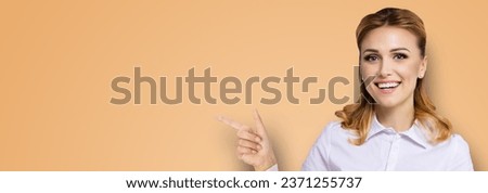 Young attractive confident woman, showing pointing finger at copy space empty text area. Success in business ad concept. Brown beige background. Wide banner composition. dental health care, healthcare