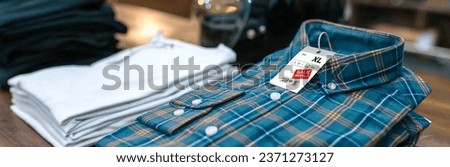 Detail of label with promotion price over a blue plaid shirt on shop with industrial style. Banner of apparel stacks ready to sell on sales season on vintage clothes store. Black friday concept.