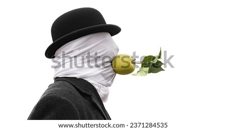 A man with a face covered by a cloth, wearing a hat and a coat, is holding an apple in his mouth without using his hands on the seashore. Royalty-Free Stock Photo #2371284535