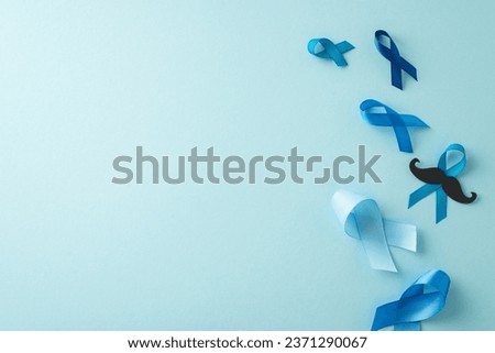 Men fighting cancer concept. Overhead view of prostate cancer emblems - blue ribbons, and mustache silhouette. Soft blue backdrop with room for text or advertising