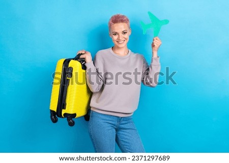 Portrait of good mood girl with short haircut wear gray clothes hold baggage green small paper plane isolated on blue color background