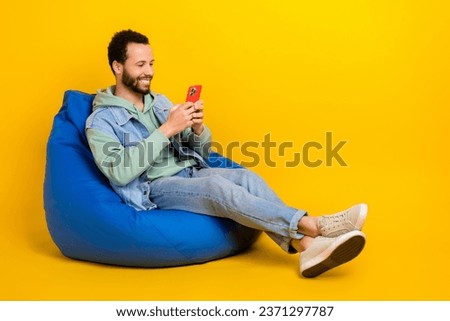 Full body size photo of smile satisfied student lying beanbag texting smartphone addicted gadget player isolated on yellow color background