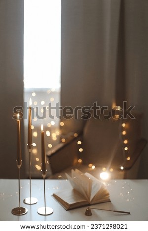 Still life details of home interior, concept of coziness and home atmosphere. beautiful golden candlesticks, scented candle, open book, garland lights. Home autumn concept, Living room Royalty-Free Stock Photo #2371298021