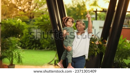 Happy Indian old grandmother holding cute little child girl in arms hands whirl dancing together outdoor home. Beautiful smiling woman sing song spinning small kid daughter enjoying summer holiday Royalty-Free Stock Photo #2371301409