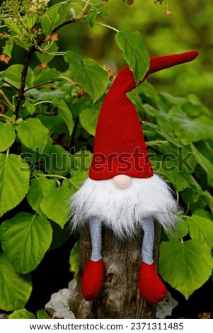 A small gnome sitting on a stone among green leaves in a garden
