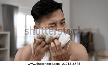 handsome asian young man is patting towel onto his clean face to dry while looking at camera like mirror during morning beauty routine at home. Royalty-Free Stock Photo #2371316575
