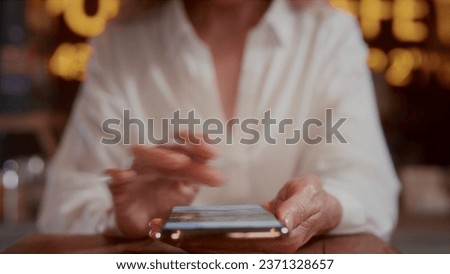 An old woman will scroll the photo on her smartphone with her hands. Senior female touches the phone screen with her fingers. Sitting in a cafe, using a mobile app. The concept of modern technologies