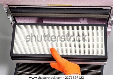Replacing filters in a home ventilation system. A hand in an orange glove changes a Hepa filter. Royalty-Free Stock Photo #2371329123