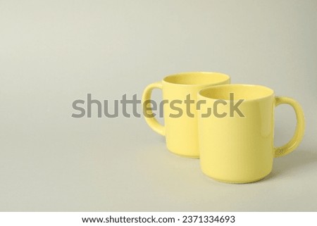 Two yellow ceramic mugs on light grey background, space for text
