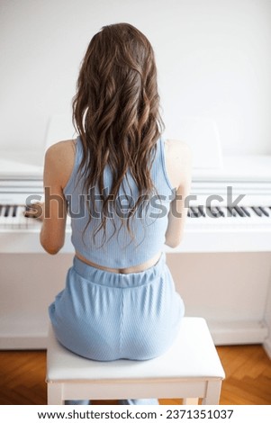 Close-up view from back of brunette woman sitting and playing piano. Practicing piano lesson at home. Concept of music and arts.