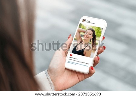 Woman looking at beautiful model's photo on mobile phone with with a slim figure. Fitness trainer social media page
