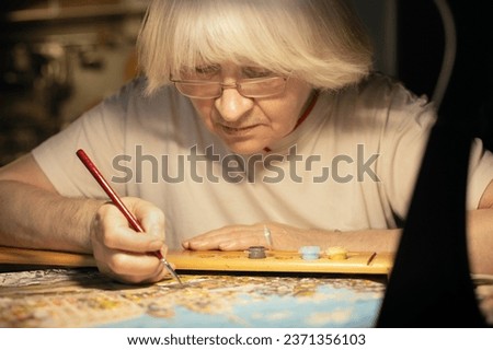 portrait of a mature woman 70 years old, artist paints a picture by numbers, hobby and creativity