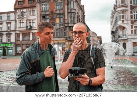 Two brothers operating a drone in an old city. One man smoking a cigarette.