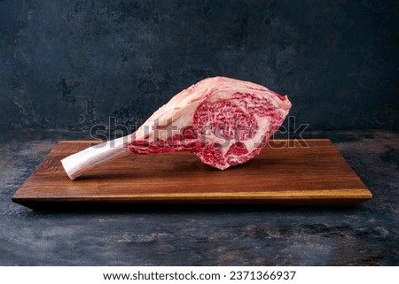 Raw dry aged wagyu tomahawk steak offered as close-up on a wooden design board with copy space  Royalty-Free Stock Photo #2371366937