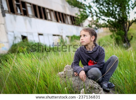 little girl sitting on a rock looking at the old house