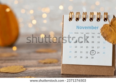 Thanksgiving Day date 2023 marked in calendar with autumn leaves, and pumpkin on wooden table with bokeh background. Close-up.