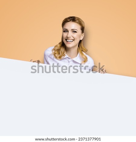 Very happy excited, laughing business woman in white confident clothing standing behind empty area banner signboard. Success and ad concept. Brown beige background. dental health care, stomotology ad.
