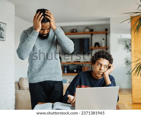 Father and son doing homework with laptop fighting and arguing over learning at home. Father and teenage son using laptop. Boy and dad sitting at home working with notebook, boy being bored  Royalty-Free Stock Photo #2371381965
