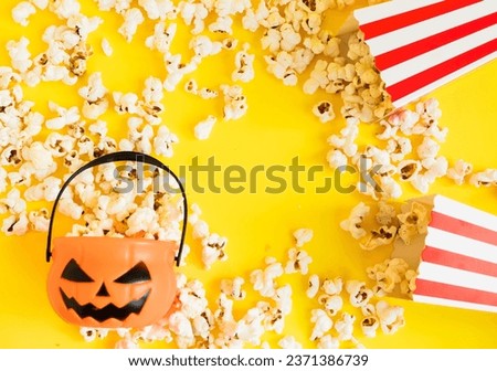 Jack o lantern basket and cinema red and white stripped boxes with popcorn on a yellow background. Halloween entertainment concept. Fall Cinema or TV watch at halloween night.