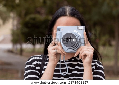 Close-up portrait of a young brunette girl on the street. She is holding a vintage Polaroid camera. A student takes pictures with a camera.