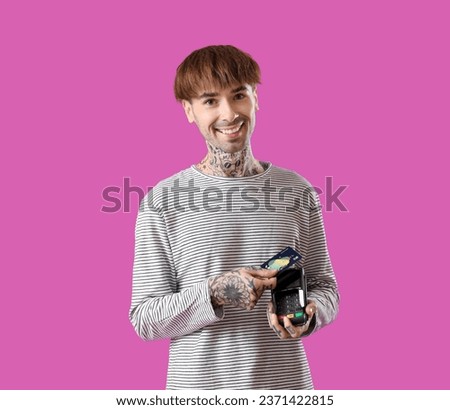 Tattooed young man with credit card and payment terminal on purple background