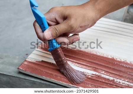 hand holding a brush applying brown colour paint on a wooden plank - painting and caring for wood with oil  
