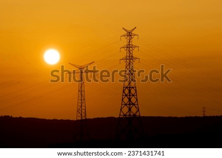 Electric pylon and the yellow sun disk setting behind it. Sunset idea concept. Natural and sustainable energy sources. Power line silhouette at sunset. Horizontal photo. No people, nobody.