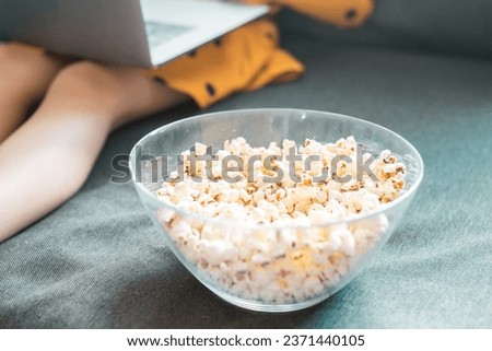 Little girl with laptop and popcorn closeup. School girl watches educational video at home. Children and cartoons concept.