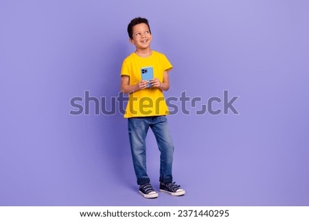 Full size photo of cute young schoolboy look empty space hold device wear yellow clothes isolated on purple color background