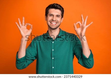 Photo of cute cheerful guy wear green shirt showing two okey signs isolated orange color background